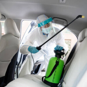 Specialist cleaner wearing personal protective equipment PPE using chemical alcohol spray cleaning inside car to decontaminate covid-19. Man in hazmat suit disinfects and cleans up auto, empty space